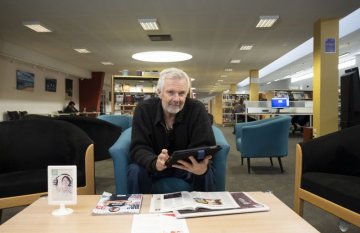 Older man with an ipad seating on chair inside Colac Library